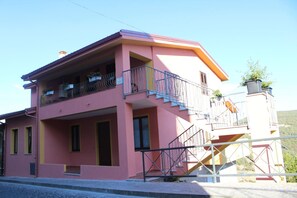 Un edificio rosa con balcón, escaleras y un pequeño jardín.