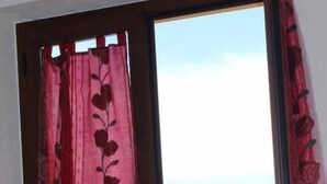 A window with a red floral curtain and a view of a hilly landscape. - B&B Tatti (Nughedu Santa Vittoria)