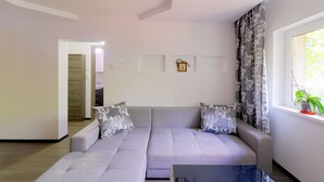 Un salon moderne avec un canapé gris, des coussins à motifs, une petite table et une fenêtre avec des rideaux.