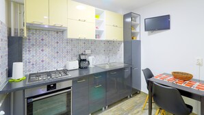 Une cuisine moderne équipée d’une cuisinière à gaz, d’un four et d’un micro-ondes encastré. On y trouve également un coin repas avec une table et des chaises, ainsi qu’un téléviseur à écran plat fixé au mur.
