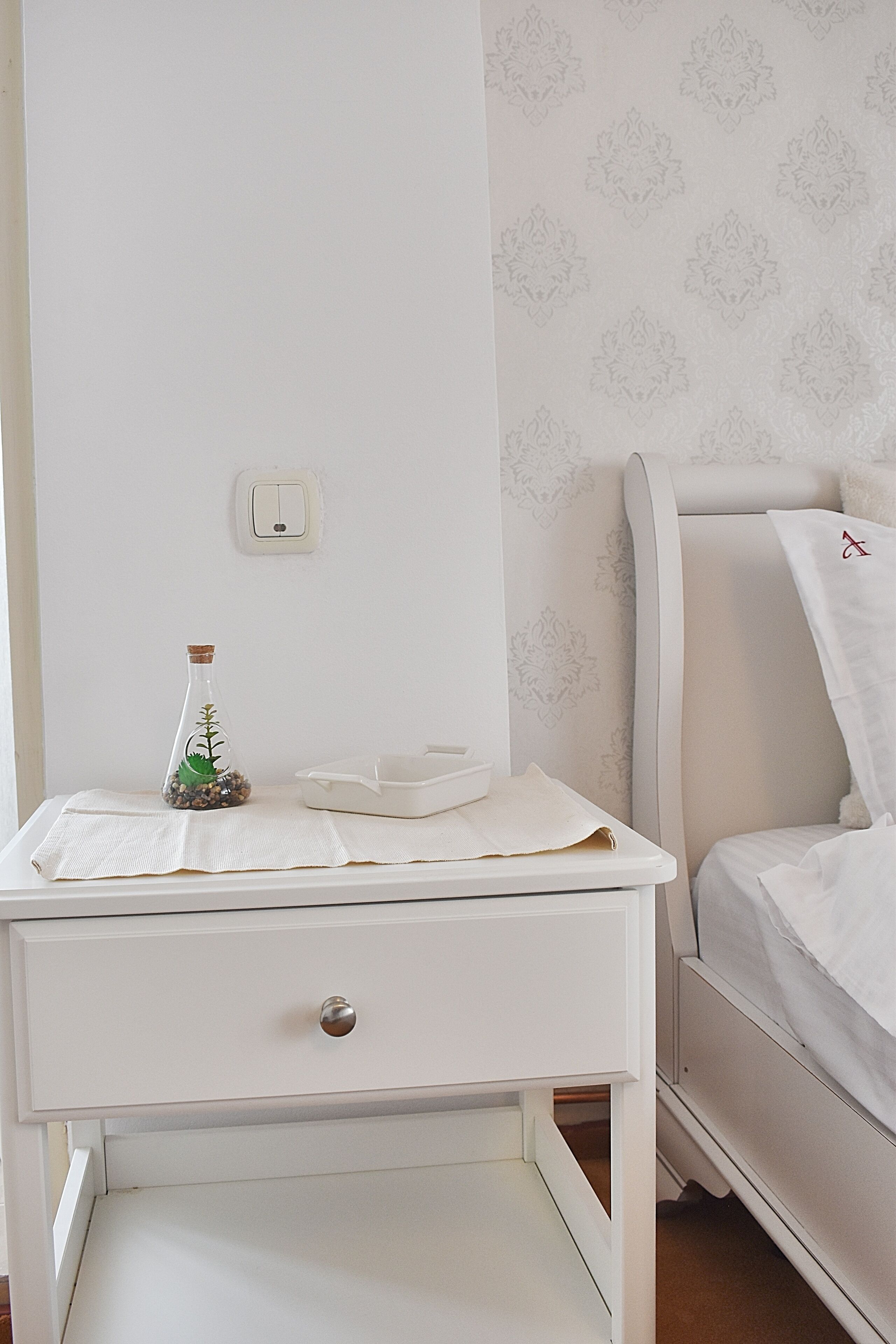 A white bedside table with a drawer, a small decorative bottle, and a tissue box.
