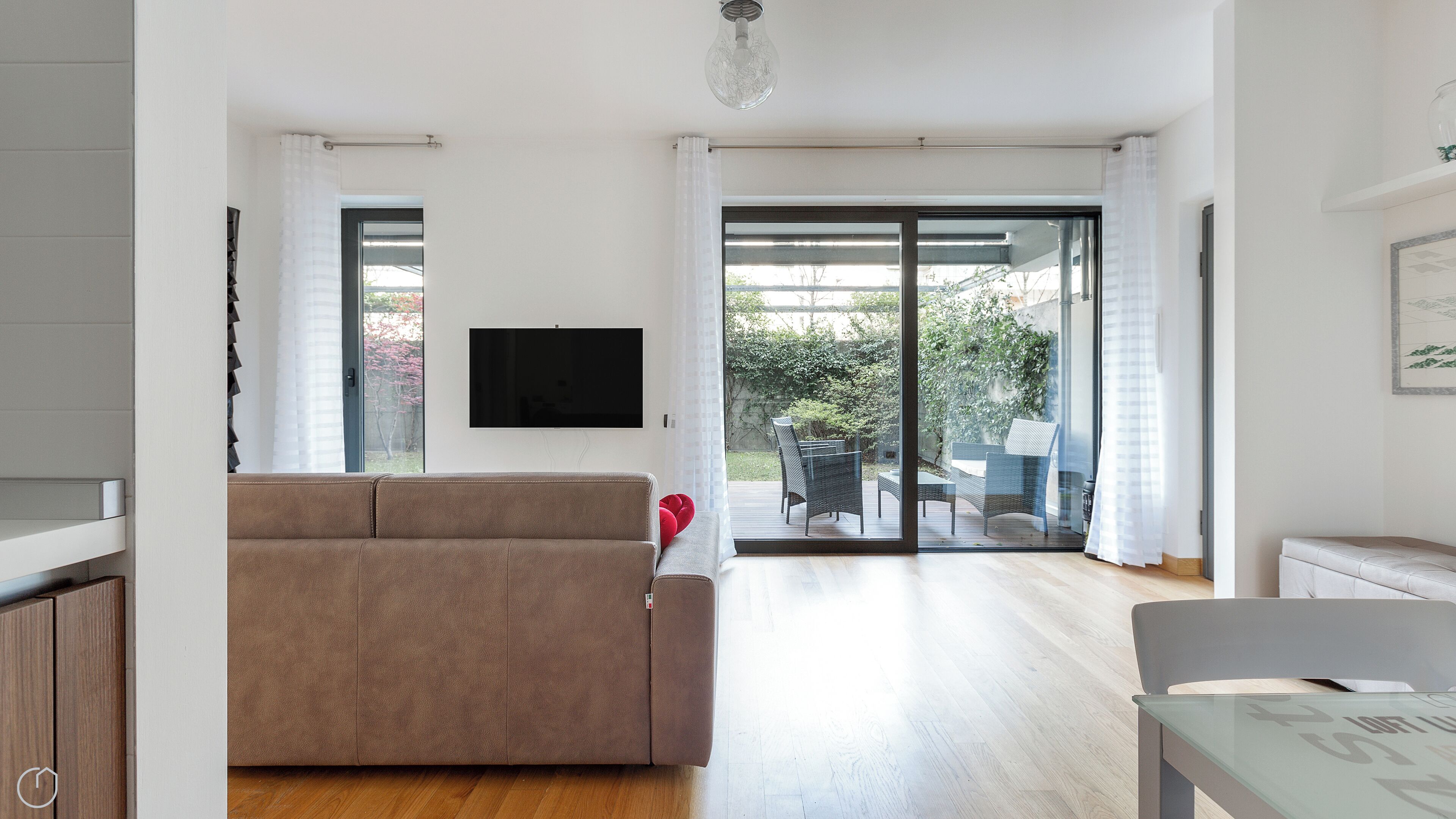 Una sala moderna con sofá, televisor de pantalla plana y puerta corrediza de vidrio que da a un patio exterior con mesa y sillas.