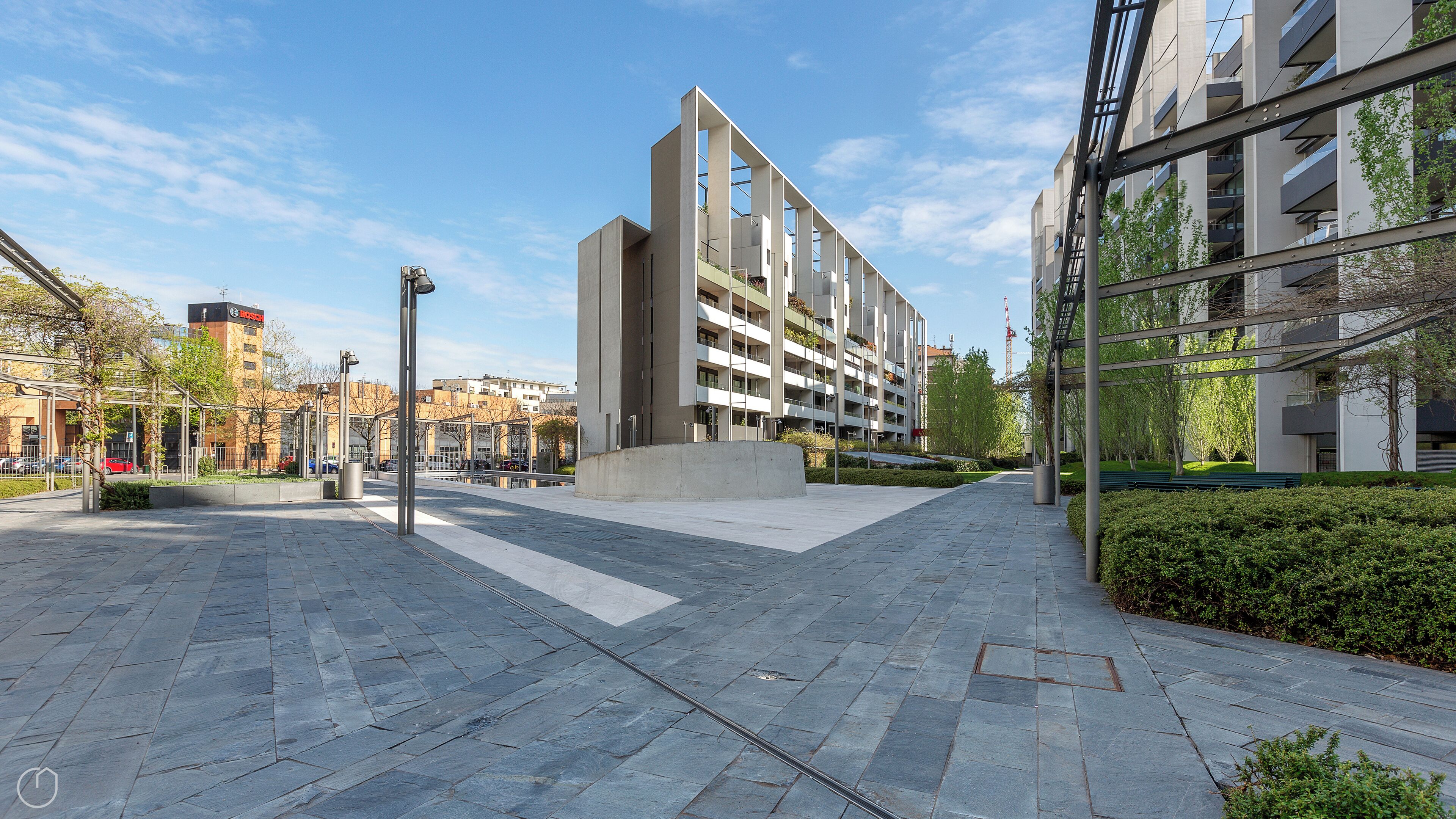 A modern urban plaza with a contemporary building featuring multiple balconies and a clear sky.