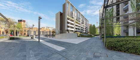 A modern urban plaza with a contemporary building featuring multiple balconies and a clear sky.