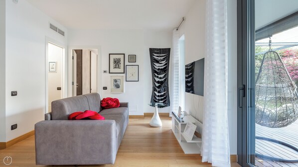 Un salon moderne avec un canapé gris, des coussins rouges, une table basse en verre et une œuvre d'art abstraite en noir et blanc accrochée au mur.