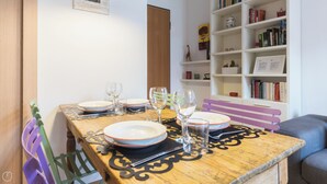 Un tavolo da pranzo apparecchiato con piatti, bicchieri e posate, una libreria con libri e oggetti decorativi, e una sedia viola.