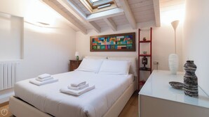 Una camera da letto con un letto, un comodino, una lampada, uno scaffale con oggetti decorativi e un'opera d'arte colorata al muro.