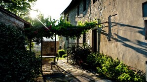 Ein Steinhaus mit rustikaler Fassade, ein Kiesweg und eine mit Kletterpflanzen bewachsene Pergola.