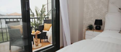 A hotel room with a balcony, a bed, a small table with a glass of juice, and a potted plant.
