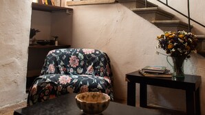 Een knus interieur met een houten bankje, een tafeltje met een schaal, een trap met een leuning, en een vaas met bloemen op een bijzettafeltje.