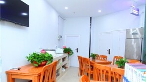 A compact dining area with wooden tables and chairs, a small kitchen area with a refrigerator, and a flat-screen TV mounted on the wall. - Vatica Beijing Chaoyang West Dawang Rd Jiulongshan Metro Station Hotel (Beijing)