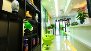 A modern reception area with a glass partition, green chairs, and decorative items on shelves. - Vatica Beijing Chaoyang West Dawang Rd Jiulongshan Metro Station Hotel (Beijing)