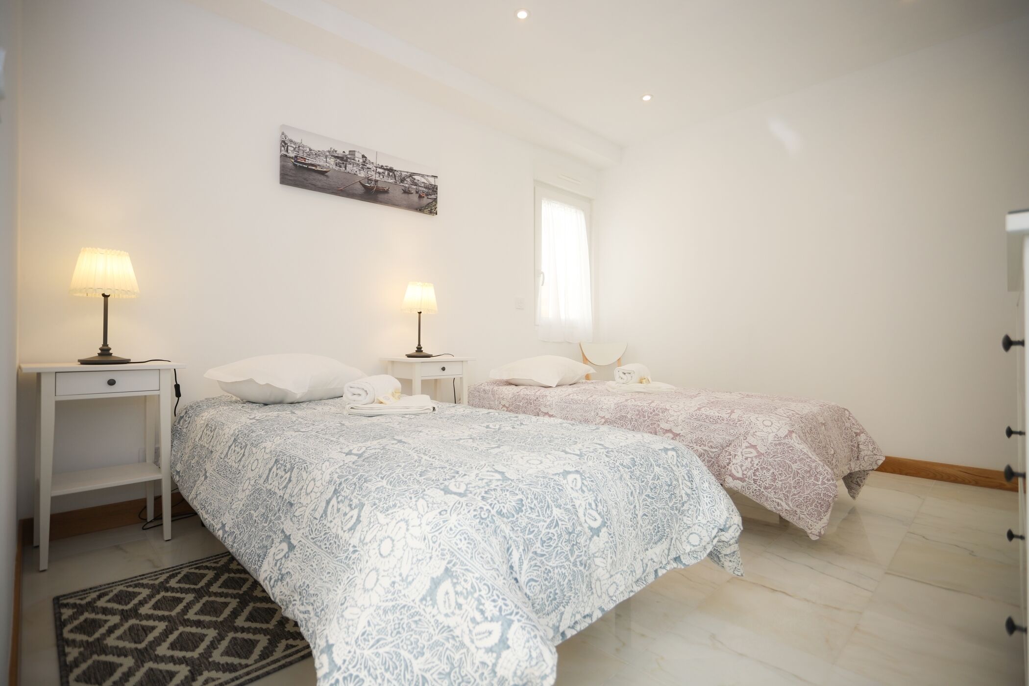 Een slaapkamer met twee bedden, een nachtkastje, een lamp, een vloerkleed en een schilderij aan de muur.