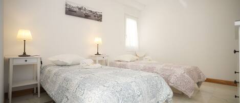 Een slaapkamer met twee bedden, een nachtkastje, een lamp, een vloerkleed en een schilderij aan de muur.