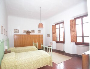 Habitación con dos camas, cabecera de madera, radiador y ventana con contraventanas de madera.