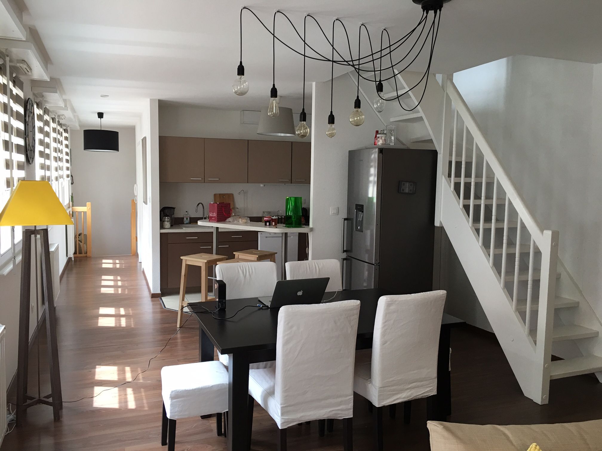 Una cocina moderna con comedor, una escalera y una lámpara amarilla.
