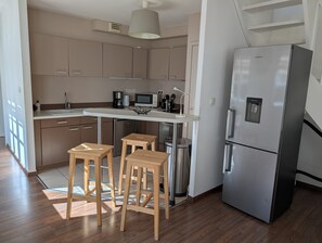 Uma cozinha moderna com geladeira de aço inoxidável, banquetas de madeira, micro-ondas e cafeteira.