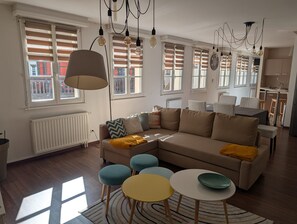 A modern living room with a sectional sofa, a dining table, and a kitchen area in the background.
