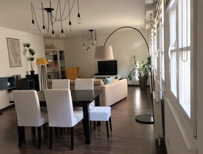 A modern living room with a sofa, dining table, chairs, a TV, and a potted plant.