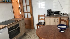 Eine kleine Küche mit Holztür, einer Kaffeemaschine, einem Toaster und einem Esstisch mit einer blauen Schüssel.