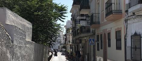 A narrow cobblestone street lined with multi-story buildings featuring balconies and a pedestrian crossing.