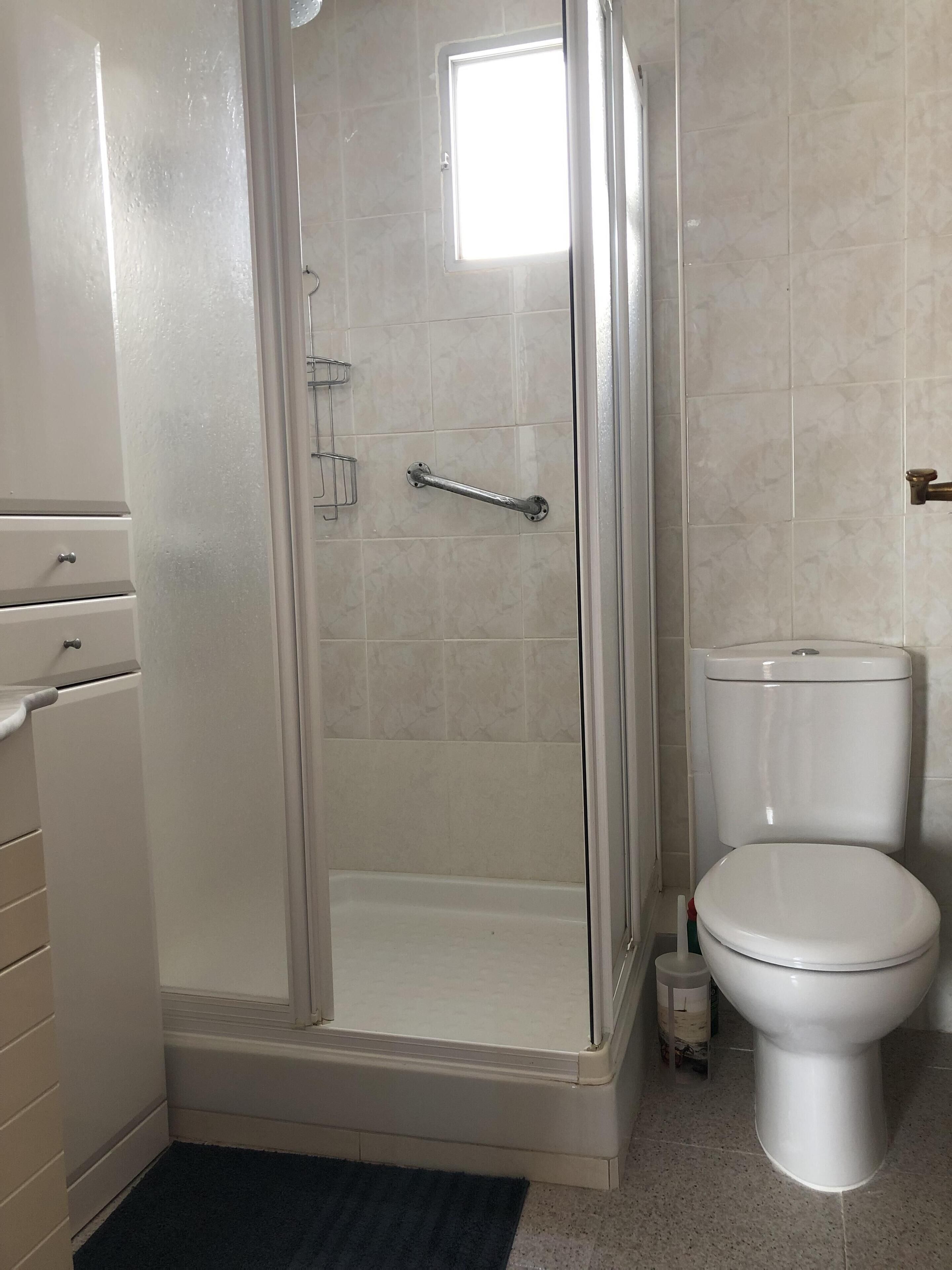 A bathroom with a glass-enclosed shower, a toilet, and a cabinet with drawers.