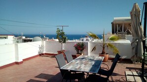 Eine Terrasse mit Tisch und Stühlen, Blumentöpfen und Blick auf das Meer.