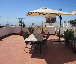 Un patio con mesa y sillas, una sombrilla y plantas en macetas.