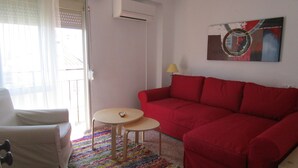 Ein Wohnzimmer mit einem roten Sofa, einem weißen Sessel, einem kleinen runden Tisch und einem farbenfrohen Teppich.
