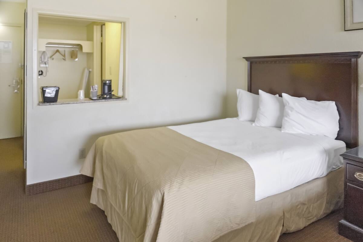 Habitación de hotel con una cama grande, un cabecero de madera, una mesita de noche, un espejo y una ventana pequeña.
