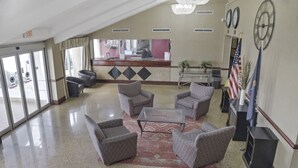 Un hall d’hôtel avec un comptoir d’accueil, plusieurs fauteuils, une table basse et une horloge au mur.