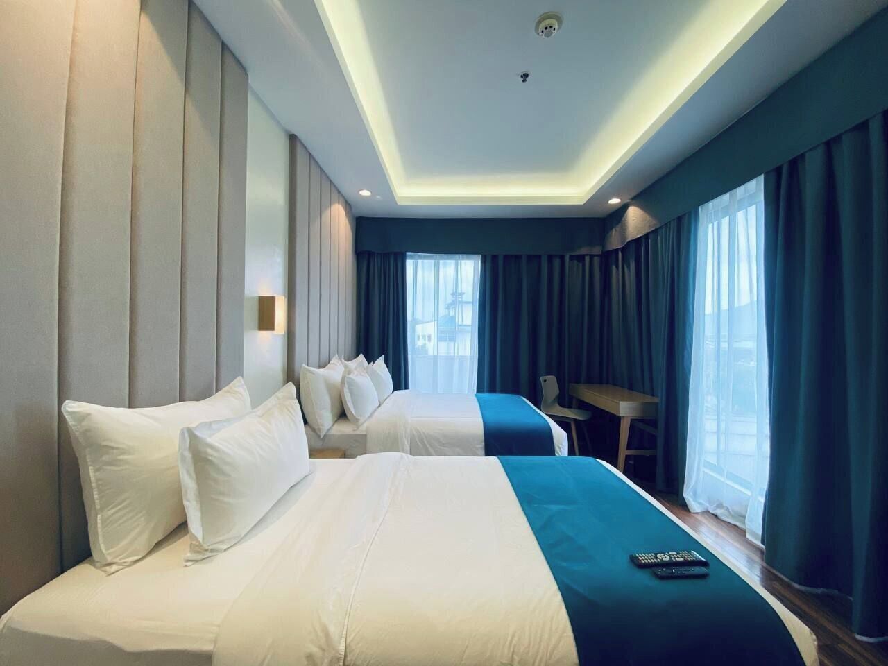 A hotel room with two beds, a desk, and a view of the city.