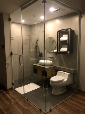 Un baño moderno con ducha envuelta en vidrio, inodoro blanco y tocador con espejo y toallero.
