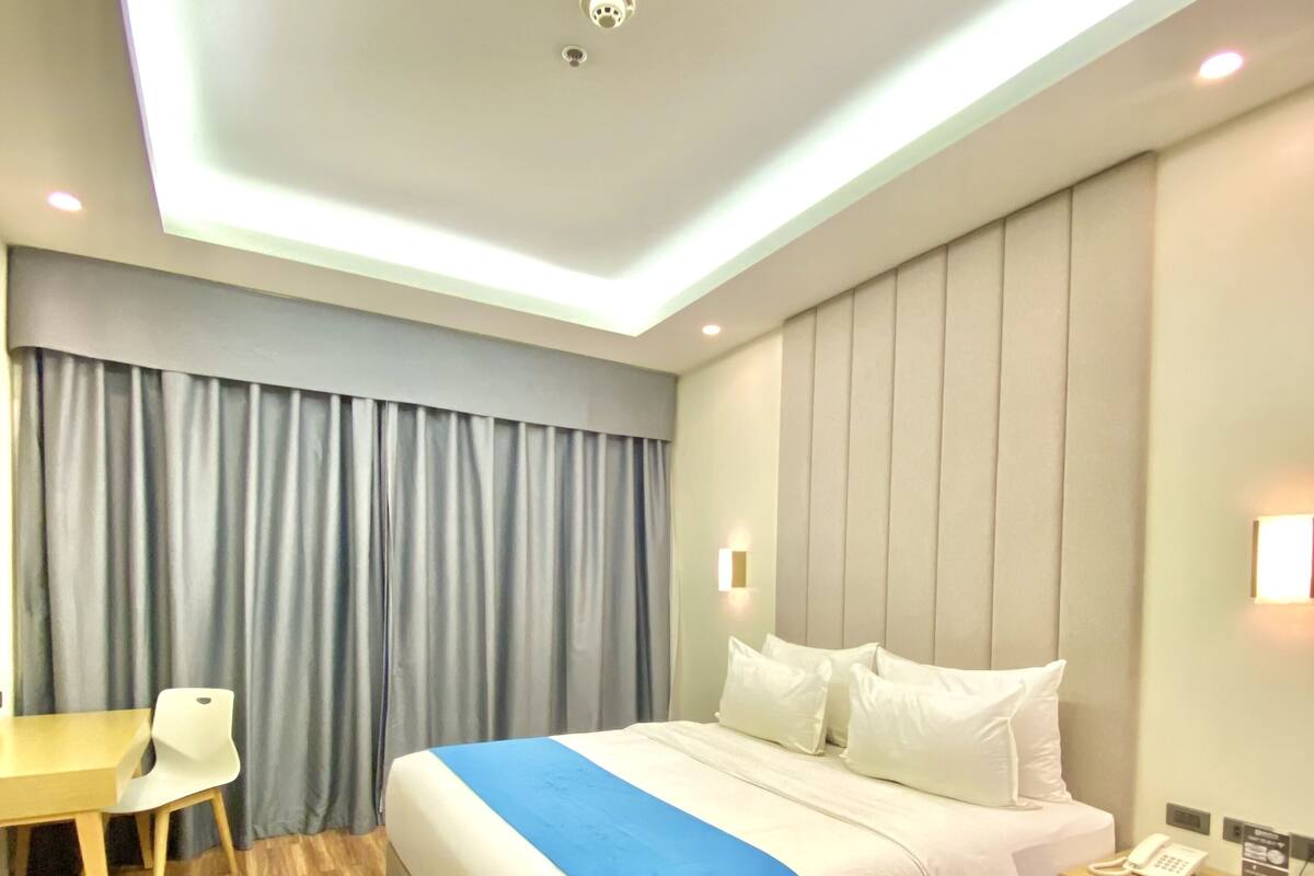 Una habitación de hotel moderna con una cama grande, un escritorio y una mesita de noche.