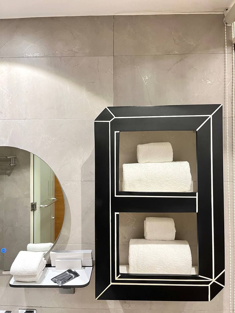 Une salle de bain avec un porte-serviettes à cadre noir sur lequel sont disposées trois serviettes, une douche en verre et un miroir.
