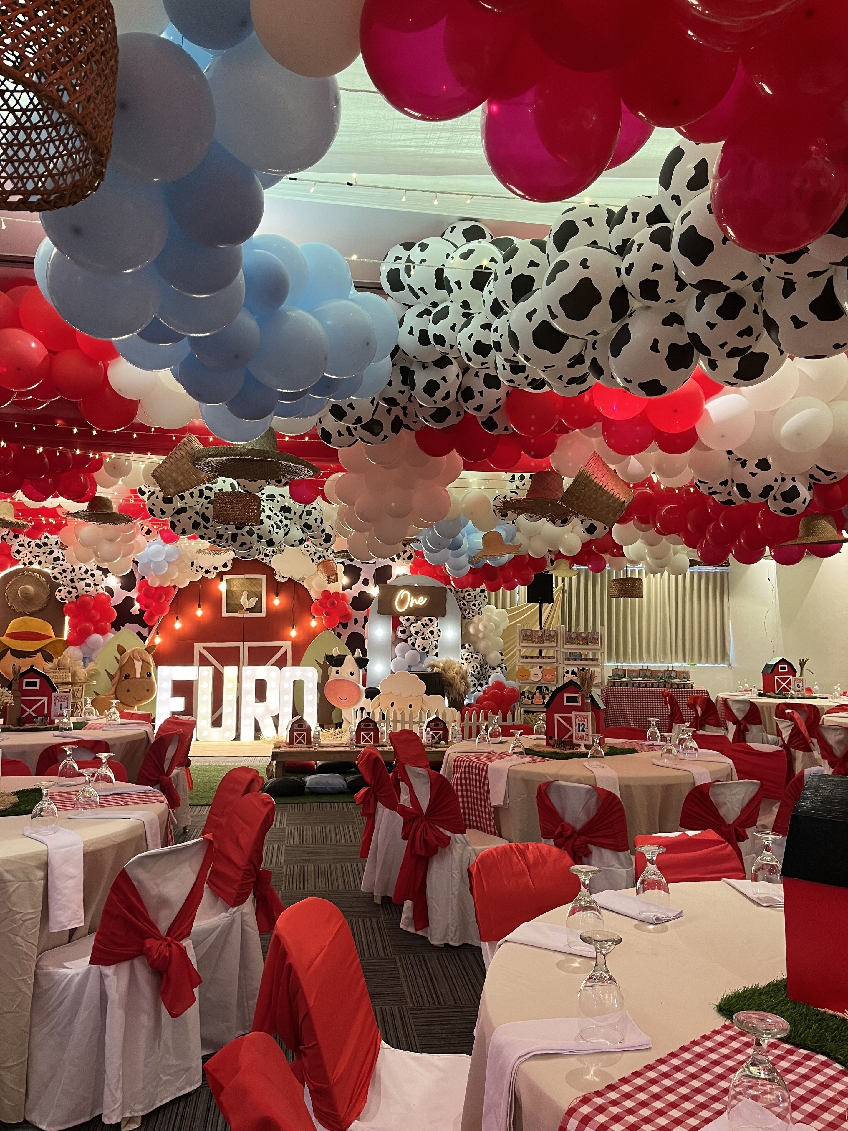 A room with tables set for a formal event, decorated with balloons and farm-themed elements.