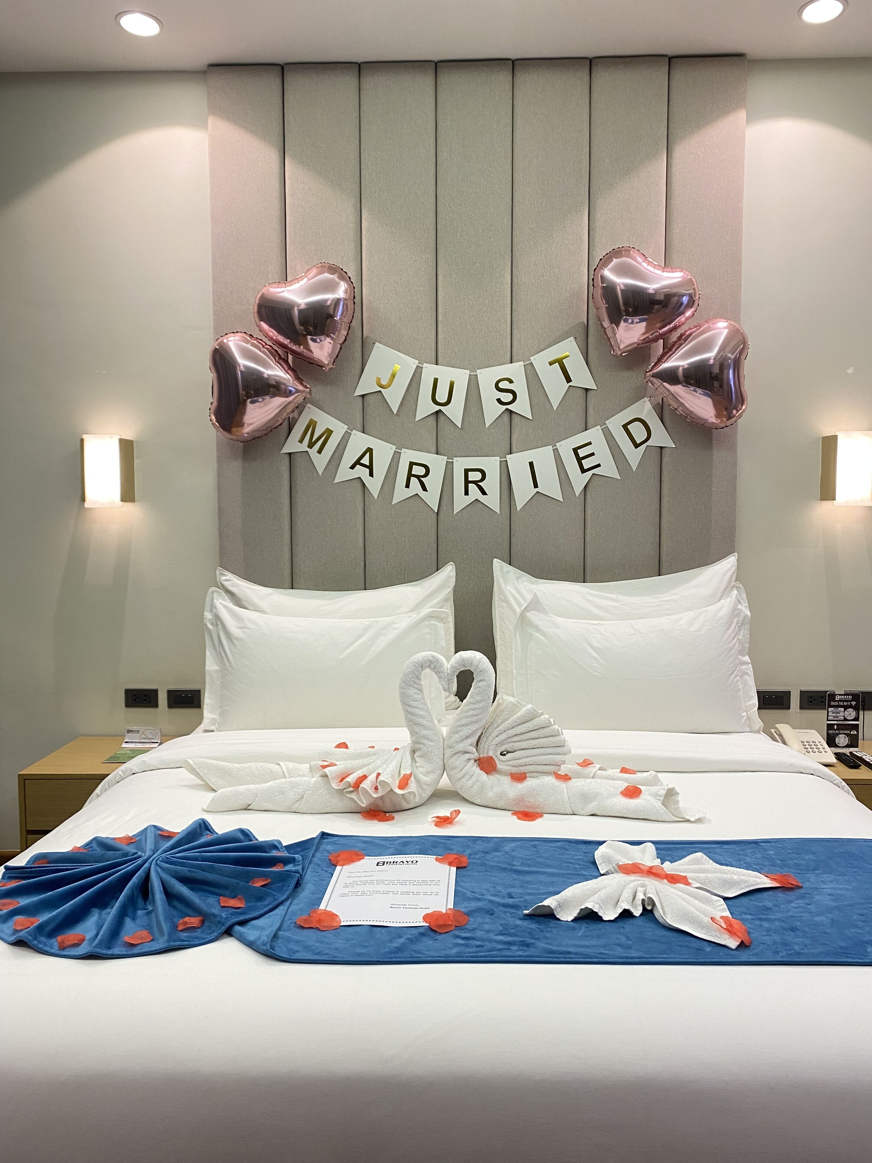 A hotel room with a bed, pillows, a decorative banner, and a swan-shaped towel arrangement.