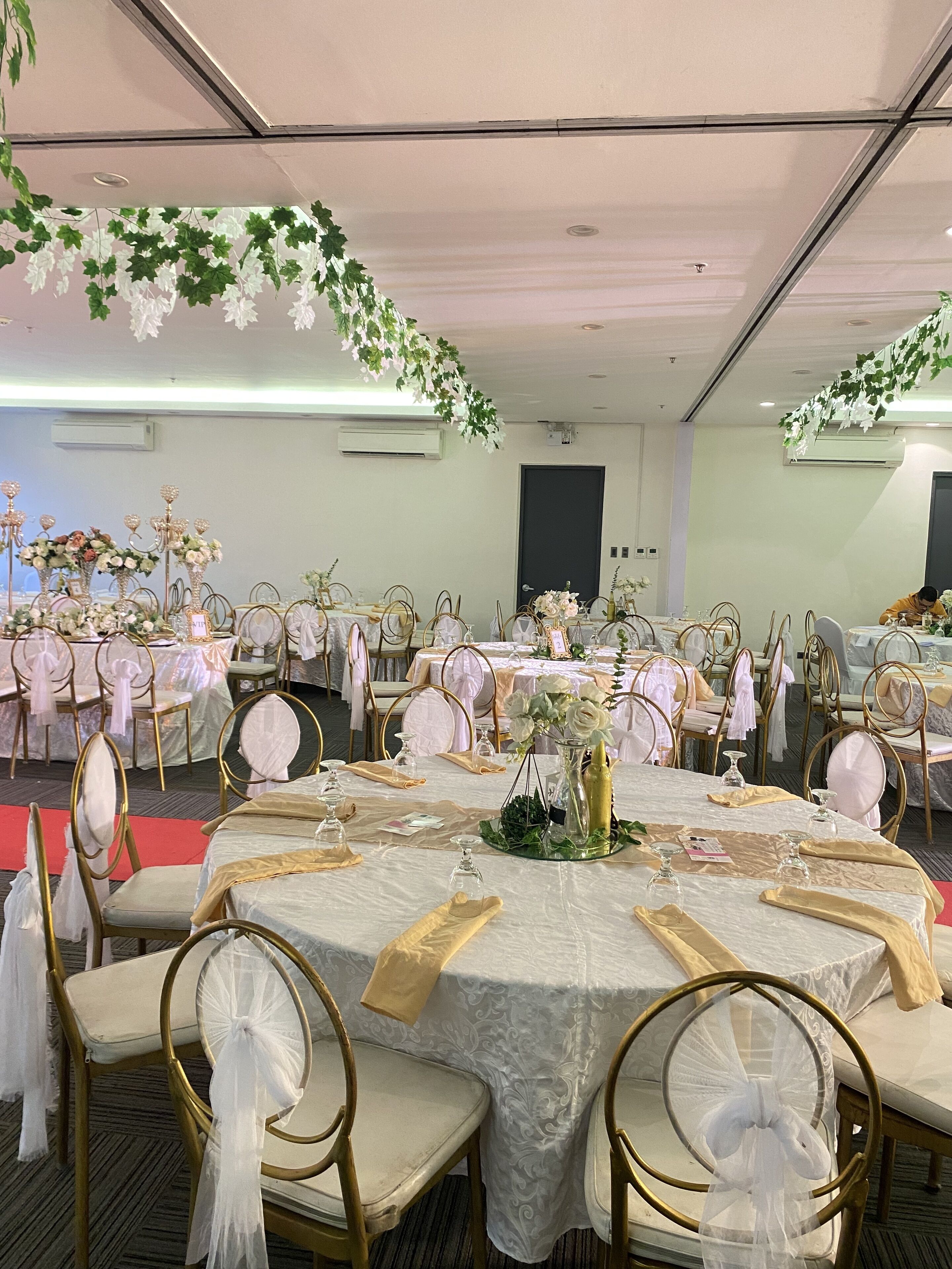 Un salón de banquetes con mesas redondas, sillas doradas y manteles blancos.
