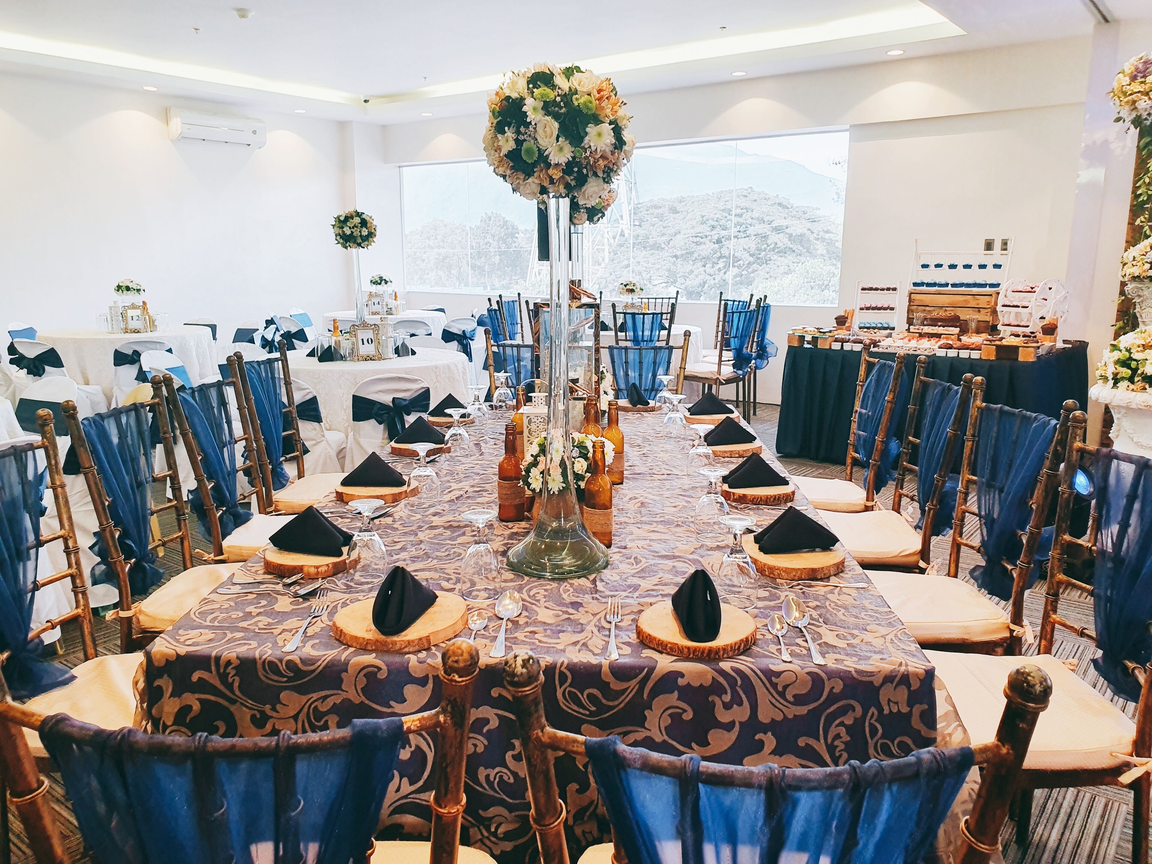 A formal dining room with round tables, blue chairs, and a large floral centerpiece.