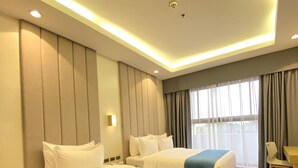 A hotel room with two beds, a desk, and a window with curtains. - Bravo Tanauan Hotel (Tanauan City)