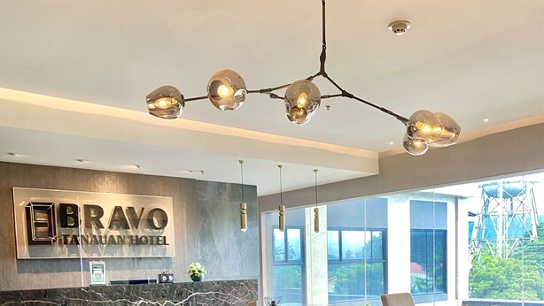 A modern lobby with a reception desk, seating area, and large windows offering a view of the outside. - Bravo Tanauan Hotel (Tanauan City)