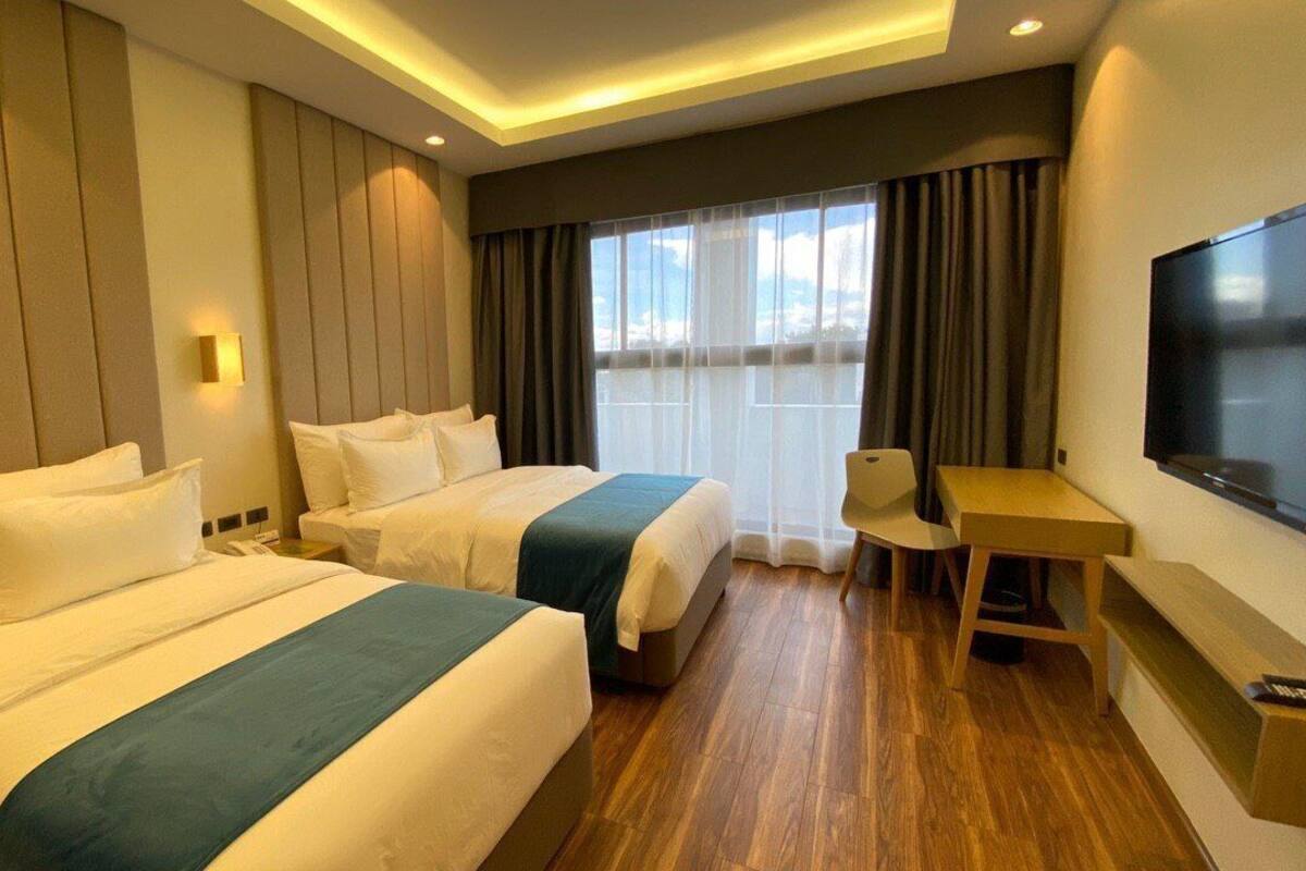 Habitación de hotel con dos camas, un escritorio y un televisor.