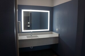 A bathroom with a white sink, a mirror with a lighted frame, and dark blue walls. - Texan Hotel (Corpus Christi)