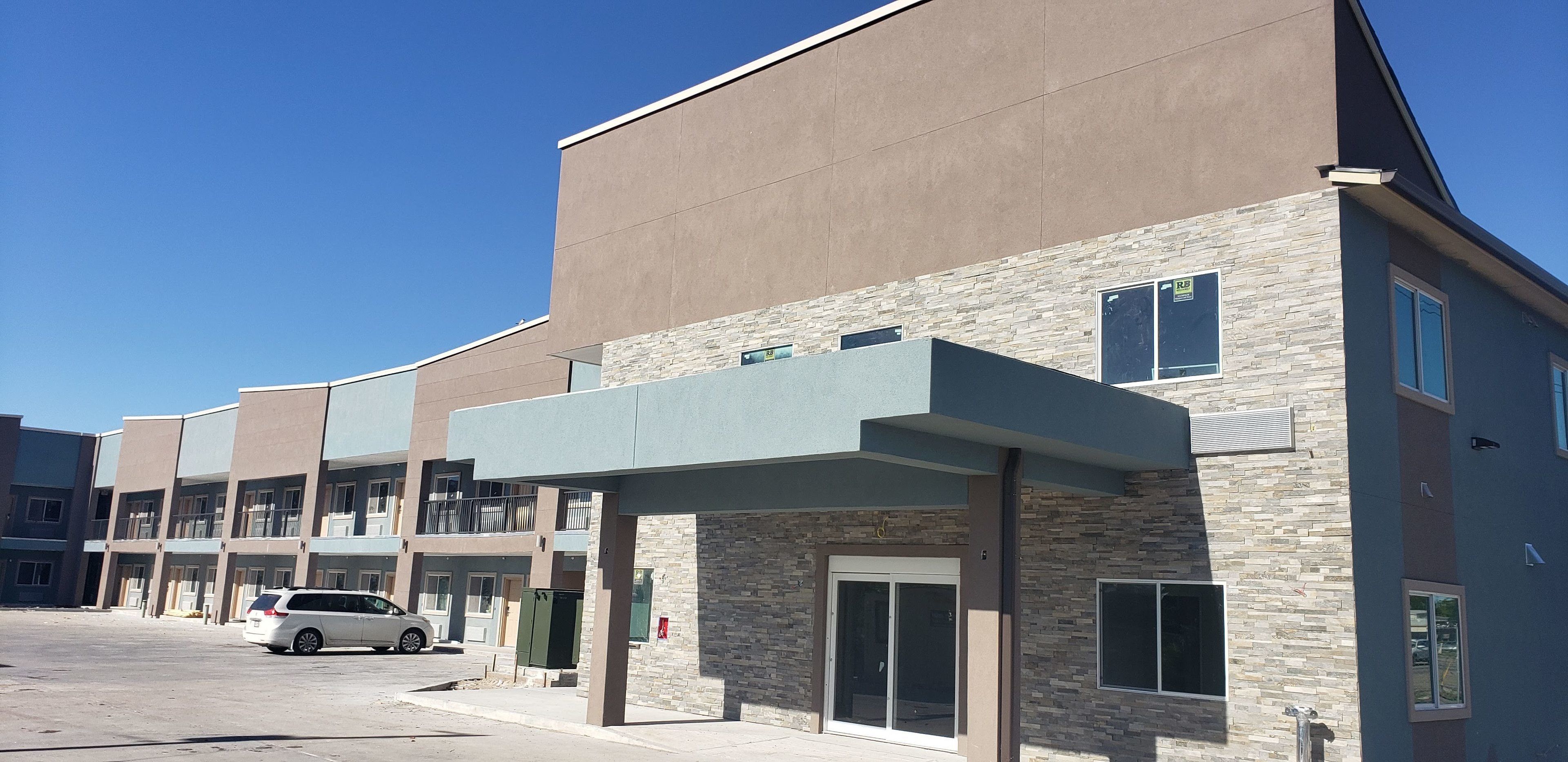 A modern multi-story building with a flat roof, large windows, and a covered entrance area.