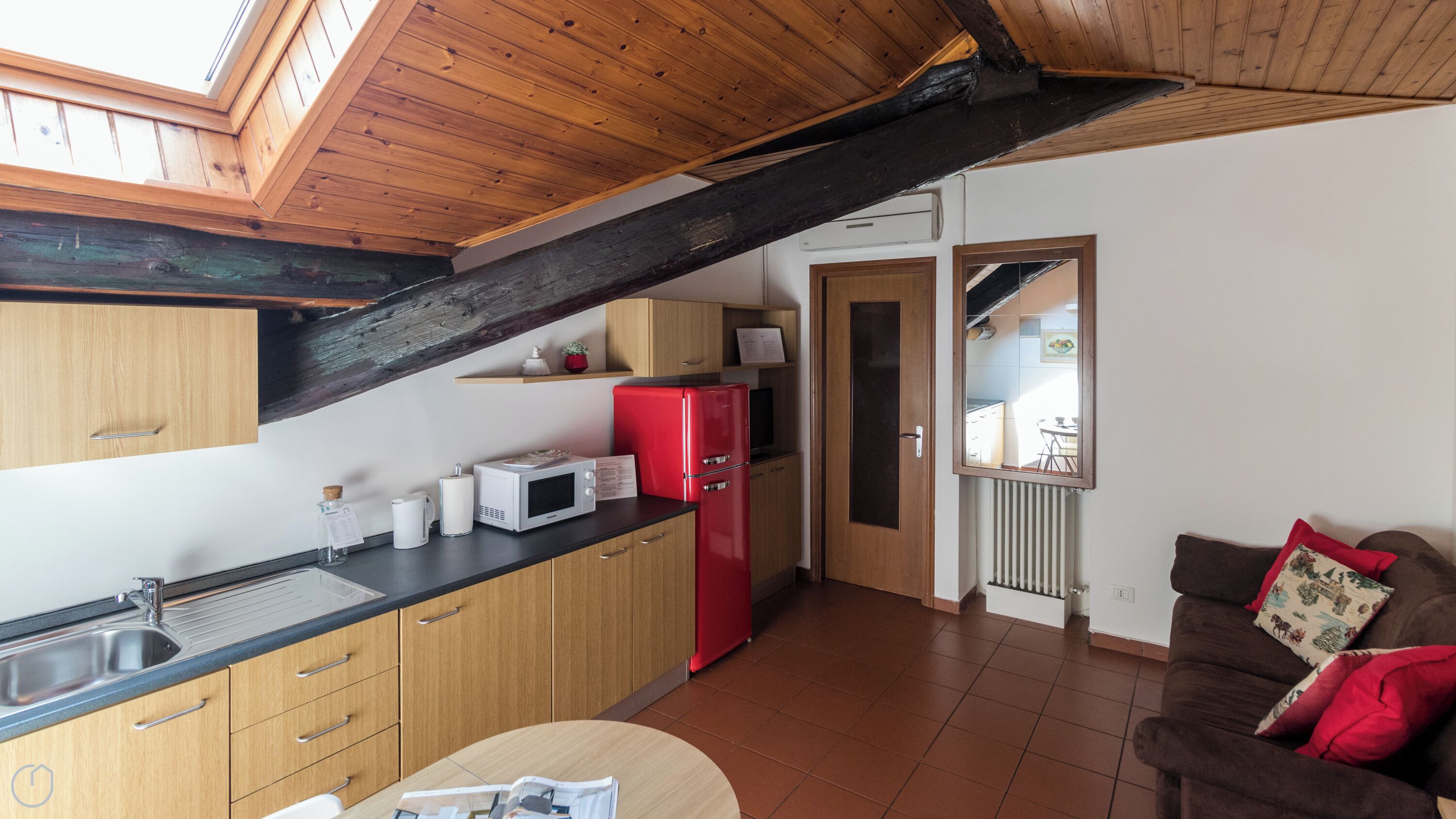 A kitchen with wooden cabinets, a red refrigerator, a microwave, and a sink.