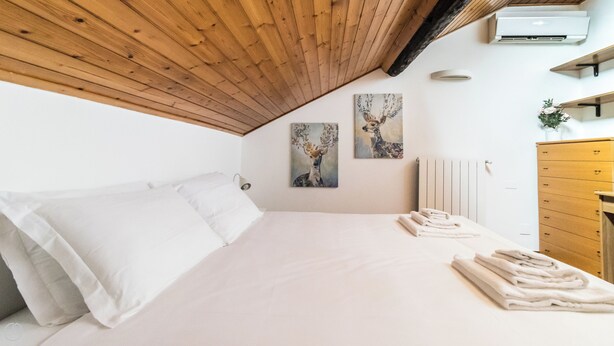 A bedroom with a wooden sloped ceiling, a bed with white linens, two wall-mounted paintings, a radiator, and a wooden dresser. - Italianway Easy - Bligny 19 C (Milan)