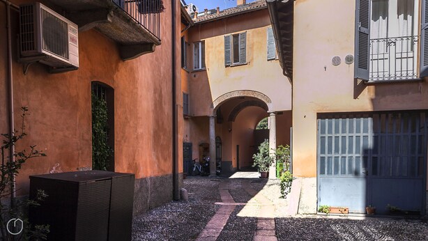A narrow alleyway with a building featuring a covered outdoor seating area, a bicycle, and a parked motorcycle. - Italianway - Ripa Ticinese 17 (Milan)