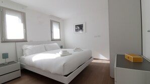 A modern bedroom with a single bed, a bedside table, a nightstand, a small desk with a chair, and a window with blinds. - Italianway - Gambara 7-6 (Milan)