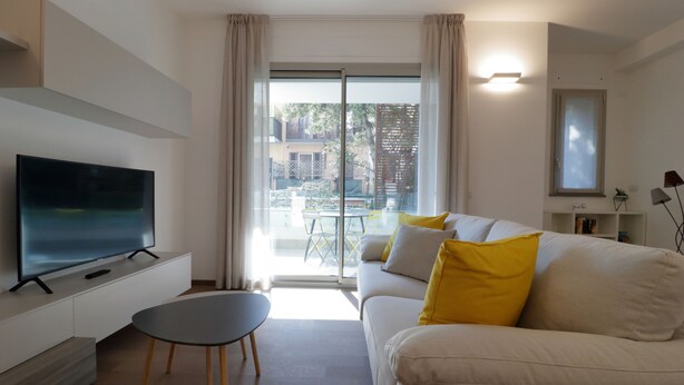 A modern living room with a flat-screen TV, a sofa with yellow cushions, a small round table, and a sliding glass door leading to an outdoor area. - Italianway - Gambara 7-6 (Milan)