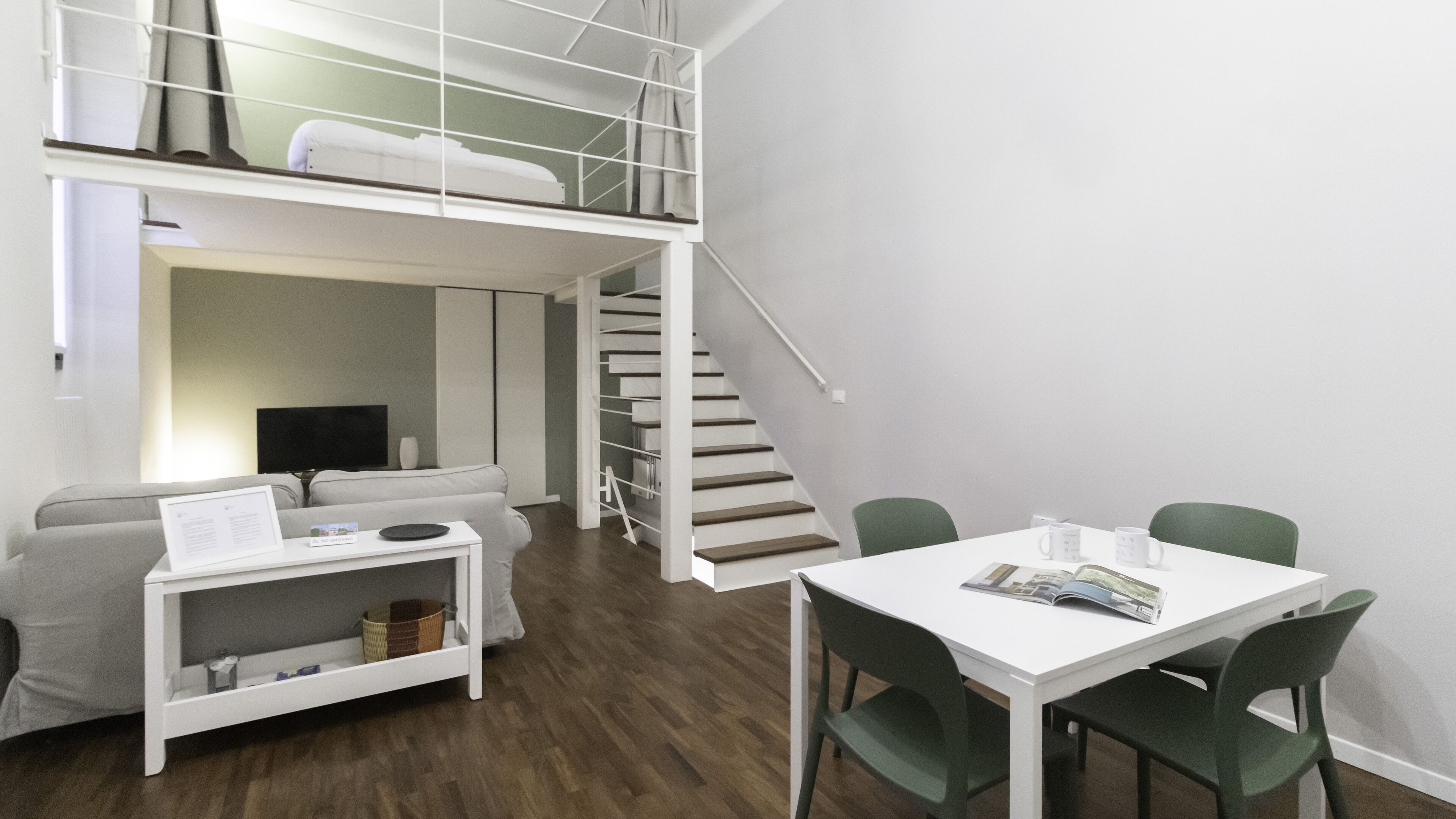 Een moderne kamer met een stapelbed, een bank, een televisie, een tafel met stoelen en een trap.